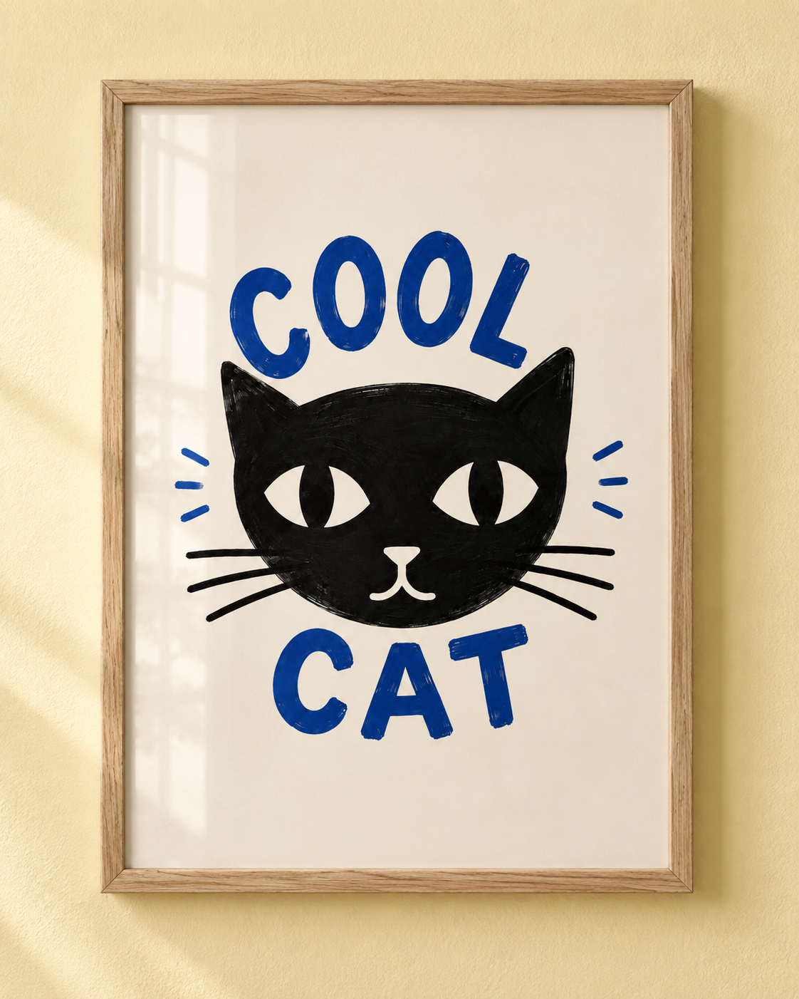 Framed wall art featuring a black cat face with the words 'COOL CAT' in blue, hanging on a warm beige wall.