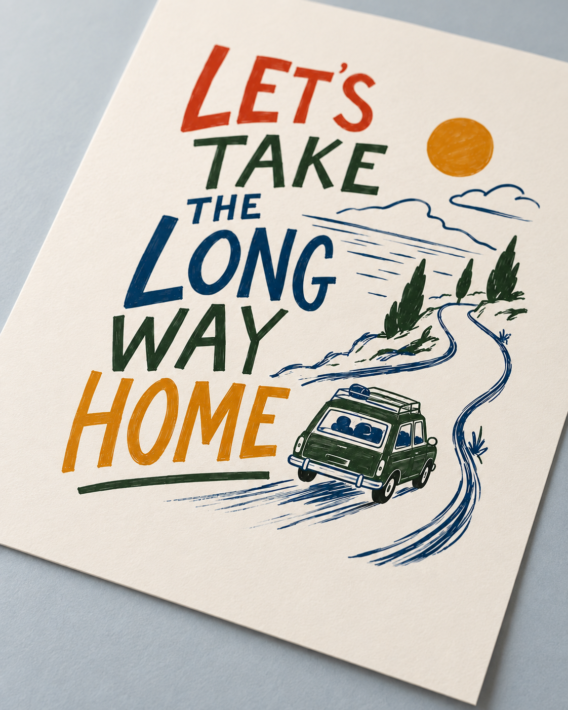 A rectangular art print with the text 'LET'S TAKE THE LONG WAY HOME' in bold retro lettering, featuring a vintage green car on a winding road, trees, clouds, and a yellow sun, photographed on a light grey surface.