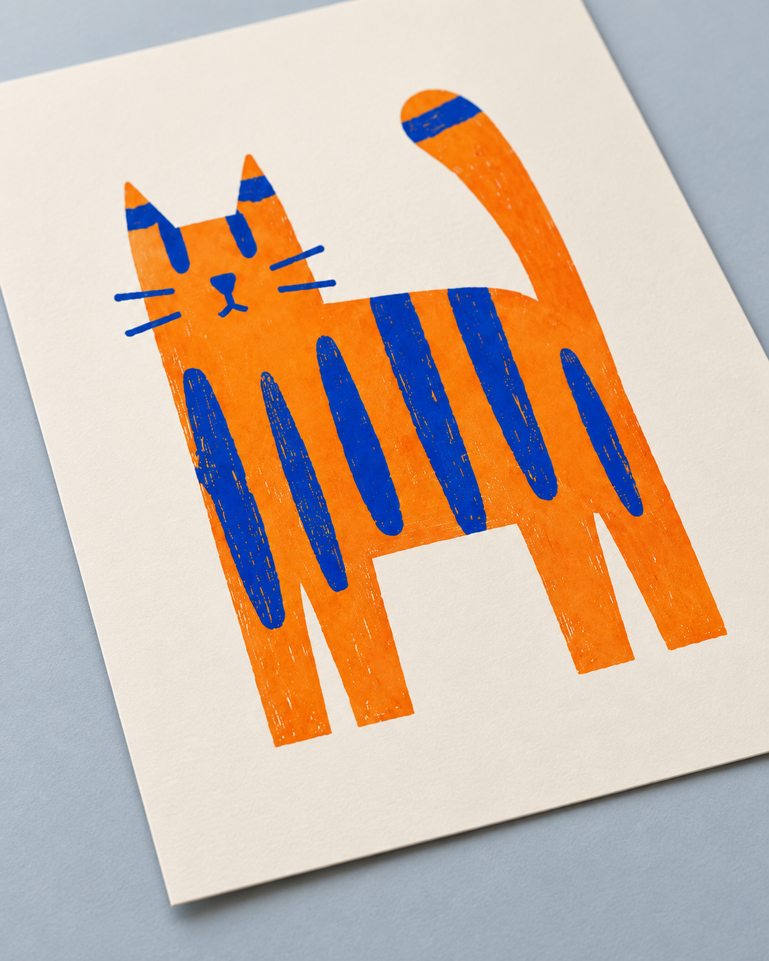 A minimalist art print of an orange cat with blue stripes, printed on a cream-colored card and photographed at an angle on a light blue-gray background.