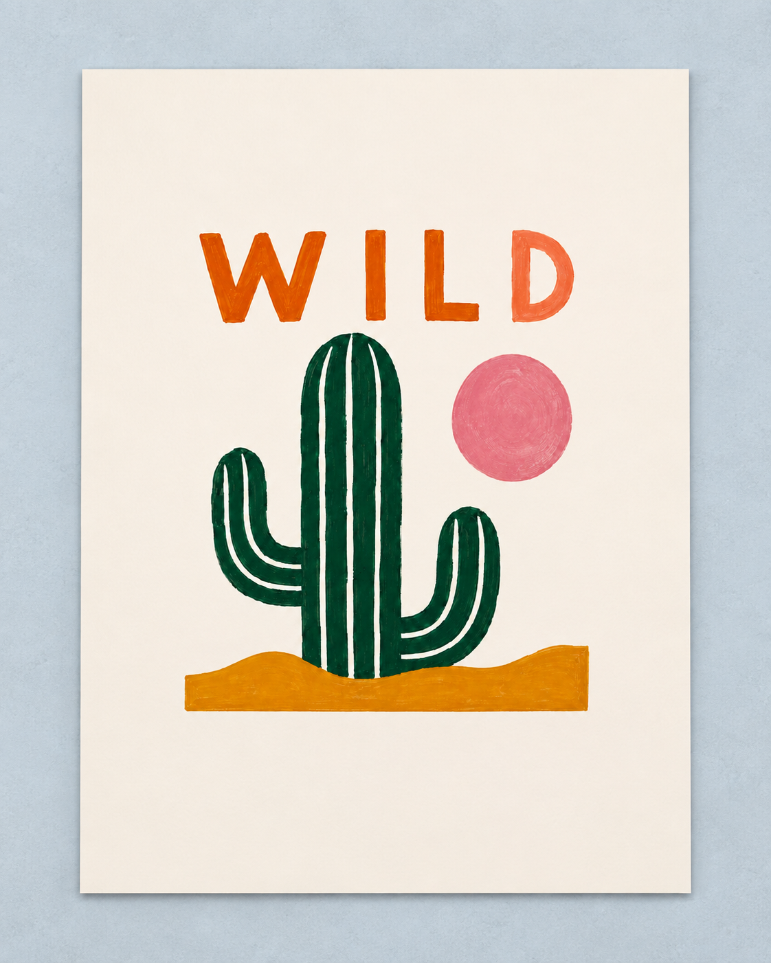 A minimalist art print featuring a green saguaro cactus, a pink sun, and the word 'WILD' in orange letters above, all on an off-white background with a light blue wall behind it.