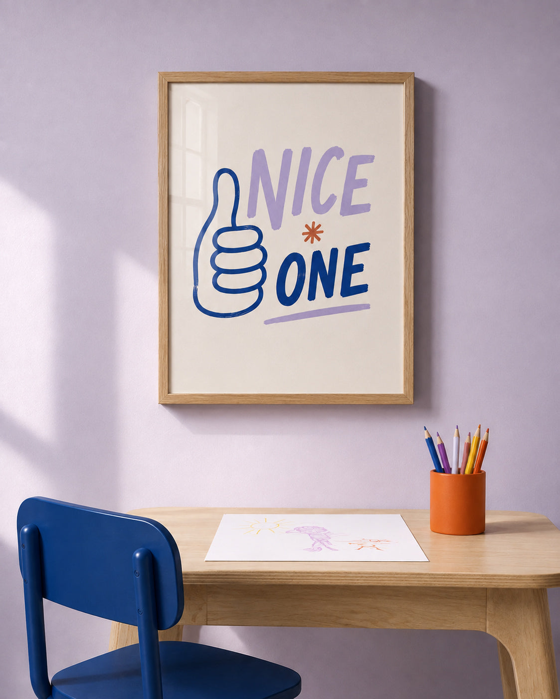 A framed wall art print with the words “NICE ONE” and a thumbs-up graphic hangs on a lavender wall above a wooden desk with a blue chair and an orange pencil cup.