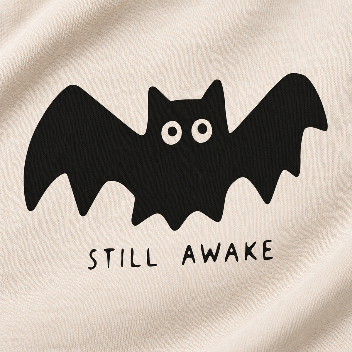Close-up of the black bat and STILL AWAKE lettering printed on cream sweatshirt fabric.