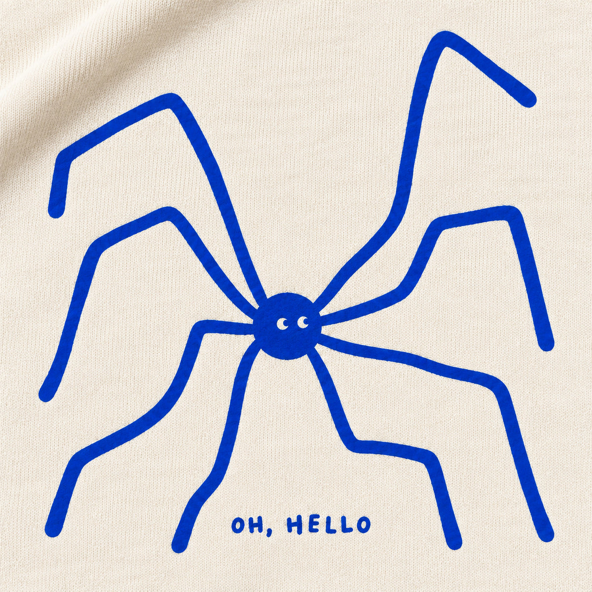 Close-up of the blue spider with eight long legs and OH, HELLO lettering on cream sweatshirt fabric.