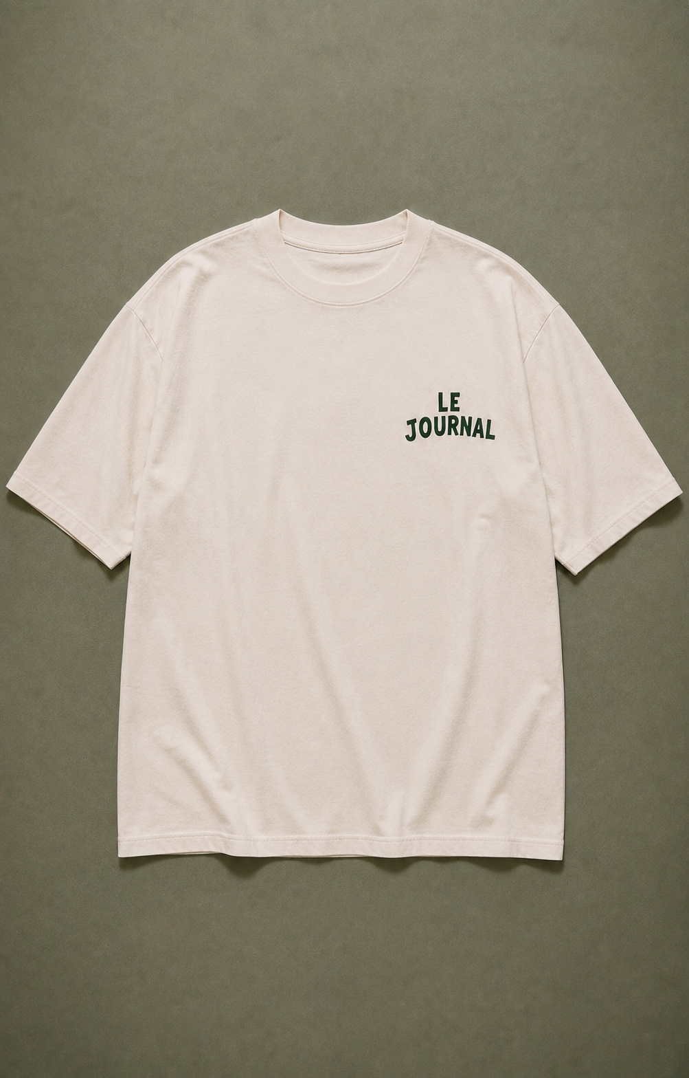 Front flat lay of the Le Journal Natural Raw oversized T-shirt with small dark green chest lettering on a sage background.